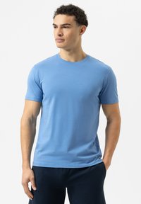 Himmelblaues T-Shirt mit kurzen Ärmeln aus weichem Material. Es hat einen runden Halsausschnitt und einen legeren Schnitt, kombiniert mit dunklen Hosen.
