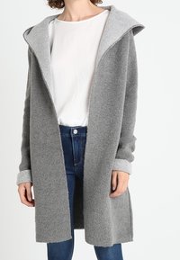 Grå lång jacka med huva, tillverkad av mjukt tyg. Den har muddade ärmar, öppen front och en avslappnad passform som ökar komforten.