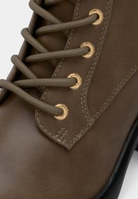 Καφέ συνθετικό δερμάτινο μποτάκι με χρυσές οπές και αντίστοιχες κορδόνες, με απαλή υφή και ενισχυμένη ραφή.