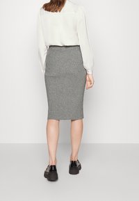 Jupe crayon en tricot côtelé gris, avec une coupe ajustée, associée à une blouse blanche à manches longues et des chaussures noires.