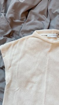 Cream-colored sleeveless top made of textured knit fabric, featuring a high neck and a tag reading "ANNA FIELD" near the neckline.