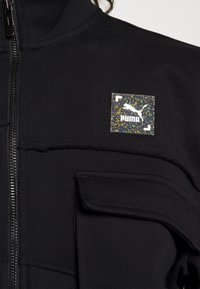 Čierna bundová mikina na zips s textúrovanou látkou, malou prednou kapsou a viacfarebným logom Puma na ľavej strane.