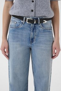 Hele sinised kõrge vöökohaga teksad, valmistatud denimist, millel on sirge sääreosa, tuhmunud pesu ja must vöö hõbedase pandlaga.