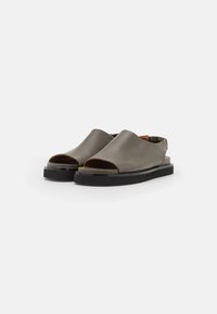 Grå läder öppen tå slip-on sandaler med svarta platta sulor och elastiska bakremmar, visade på en vit bakgrund.