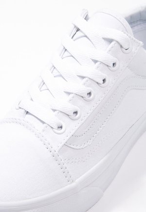 Nærbillede af hvid canvas-sneaker med hvide snørebånd og detaljeret syning på siden og tåområdet.
