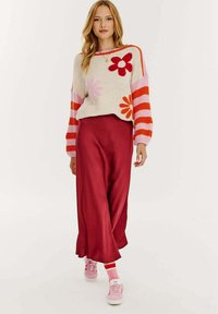 Sweter robiony na drutach z kolorowymi kwiatowymi wzorami w odcieniach różu, czerwieni i pomarańczu; w zestawieniu z długą burgundową spódnicą; różowe trampki z białą podeszwą.