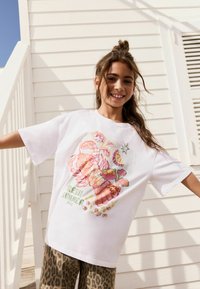 Fehér, rövid ujjú póló színes tengeri ételekkel díszítve, többek között homárral és rákokkal, valamint a "FRESH SUMMER DAYS" felirattal. Leopárdmintás nadrággal párosítva.