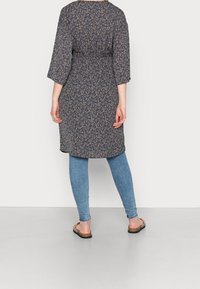 Blaues, floral gemustertes Kleid mit Dreiviertelärmeln, tailliertem Schnitt und lockerer Passform, kombiniert mit hellblauen Skinny-Jeans und Sandalen.