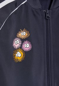 Close-up of navy blue jacket with zipper and cartoon-style colorful fuzzy creatures with eyes printed near the chest.