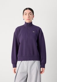 Paarse fleece pullover met een hoge kraag, kwart rits, ribgebreide manchetten en zoom. Bevat een klein groen logo op de borst.