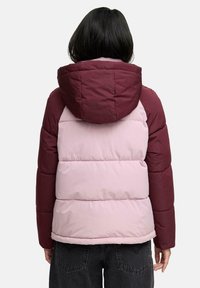 Veste matelassée avec une capuche et des manches bordeaux, un corps rose clair, du matelassage et des poignets élastiques. Elle dispose d'une capuche avec cordon de serrage.
