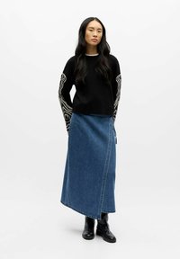 Svart genser med hvitt abstrakt mønster på ermene, kombinert med en lang denimskjørt og svarte ankelstøvler. Glatt stoff, avslappet passform.