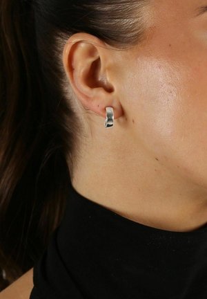 Silver hoopsmycke som visas på ett delvis synligt öra, med en slät, polerad yta och en enkel, rundad design.