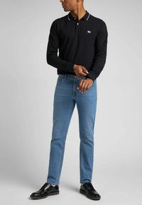 Zwarte polo met lange mouwen en witte kraagaccenten, gecombineerd met lichtblauwe denim jeans en zwarte veterschoenen, met een getailleerde pasvorm.