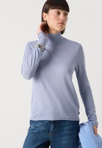 Light blue turtleneck sweater in soft fabric with long sleeves. Features a fitted silhouette and subtle ribbing. Worn with blue jeans.