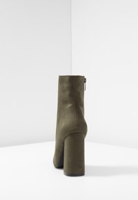 Bottine en velours vert olive avec un talon carré, dotée d'une fermeture éclair sur le côté et d'une texture lisse. Design minimaliste avec des lignes épurées.