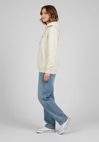 Felpa crema con tasca frontale, vestibilità rilassata. Abbinata a jeans azzurri chiari e sneaker bianche. Tessuto morbido e polsini a costine.