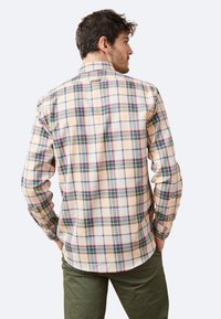 Camisa de cuadros para hombre en beige, con un patrón de cuadros multicolor que incluye acentos en azul, rojo y verde; de manga larga y con dobladillo curvado.
