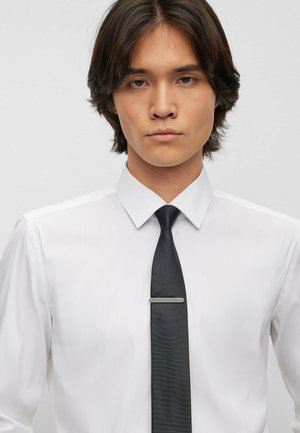 White dress shirt with a classic collar, paired with a black tie featuring a textured finish and a silver tie clip.
