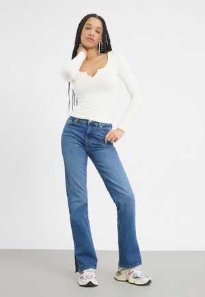 Witte lange mouwen top met een gegolfde halslijn, gecombineerd met hoge blauwe denim jeans met een rechte pijp en zijsplitten.