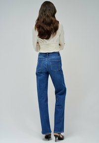 Jeans de mezclilla azul de cintura alta con un corte relajado, que cuentan con dos bolsillos traseros y sutilezas en la costura. Combinados con una blusa ligera y con fruncidos.