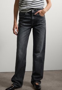 Jeans rectos negros de mezclilla, con un dise�ño clásico de cinco bolsillos y cierre de botón, combinados con una blusa a rayas y zapatos planos negros.