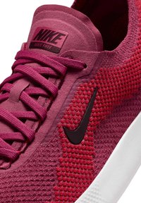 Nike Free -kengät syvänpunaisena, jossa on teksturoitu verkkopäällinen, litteät nauhat ja musta swoosh-logo valkoisen pohjan päällä.