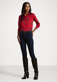 Red button-up shirt featuring a colorful botanical print, paired with dark denim jeans and knee-high black leather boots.