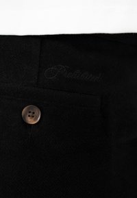 Tissu noir avec un seul bouton marron à quatre trous et une légère broderie cursive près du bord supérieur.