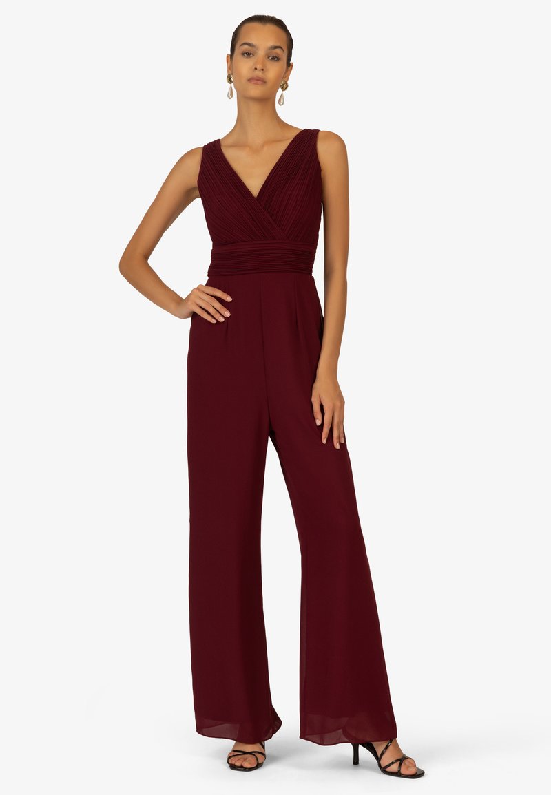 Bordeauxfarbener Jumpsuit mit V-Ausschnitt, gefaltetem Oberteil und weit geschnittenen Hosen. Aus glattem Stoff gefertigt, mit eleganten Drapierungsdetails.