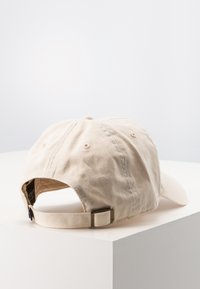 Casquette de baseball beige avec une visière courbée, fabriquée en coton, avec des détails cousus et une sangle ajustable à l'arrière.