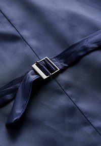 Marineblauem Stoff mit glatter Textur, versehen mit einem Satin-Gürtel, der mit einer rechteckigen silbernen Schnalle gesichert ist. Klare Linien und minimales Design.