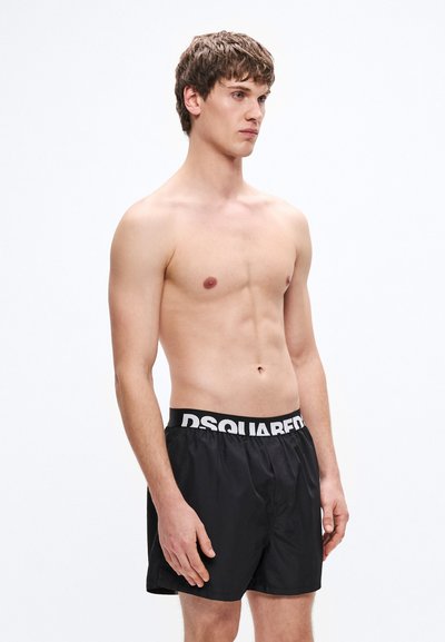 Bañador negro con cintura elástica blanca con el logo de la marca. El bañador es ligero, de textura suave y corte holgado.