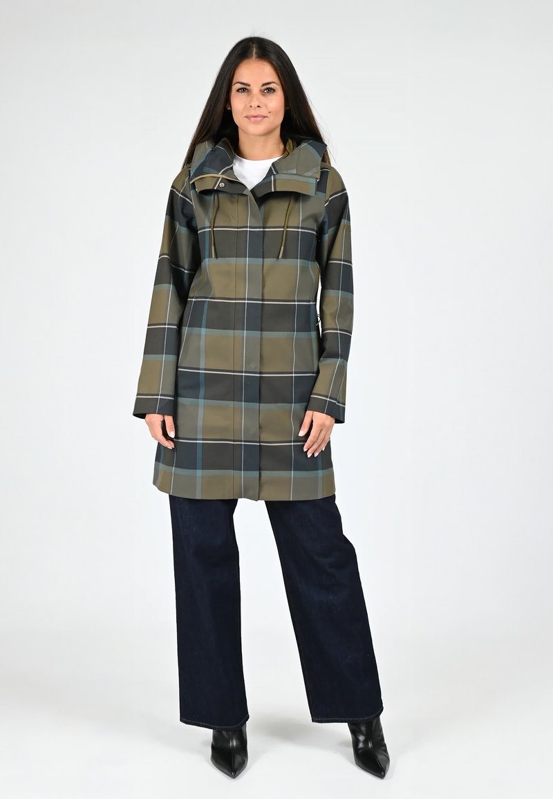 Imperméable à carreaux en olive et noir, doté d'une capuche, d'un cordon de serrage et d'une coupe droite. Porté sur un jean large sombre et des bottes à talons noires.