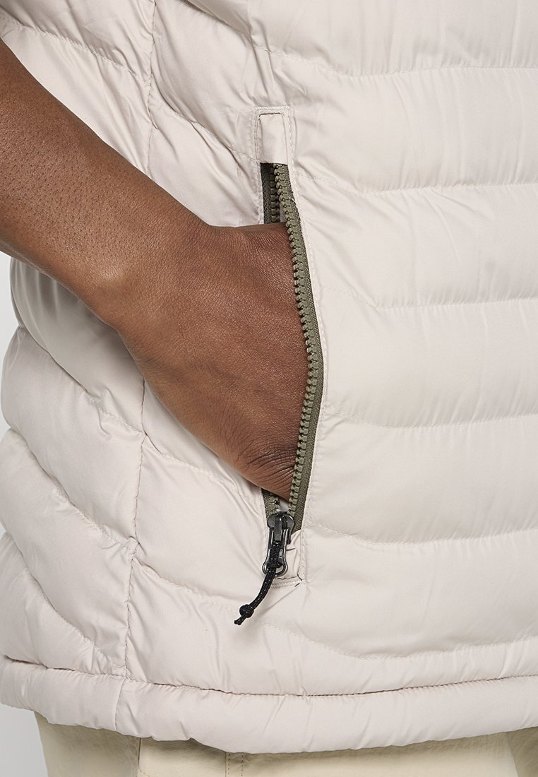 Gilet imbottito leggero in morbido tessuto beige con texture trapuntata. Presenta una tasca con zip rifinita in verde oliva per un uso funzionale.