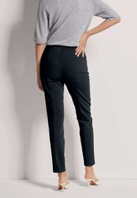 Zwarte, op maat gemaakte broek met een slim fit, gemaakt van een soepel, rekbaar materiaal. Gepaard met lichtgekleurde, open-toe hakken.