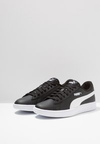 Sneaker athletic neri in pelle sintetica, con una striscia bianca, lacci neri e un interno texturizzato. Suola in gomma bianca.