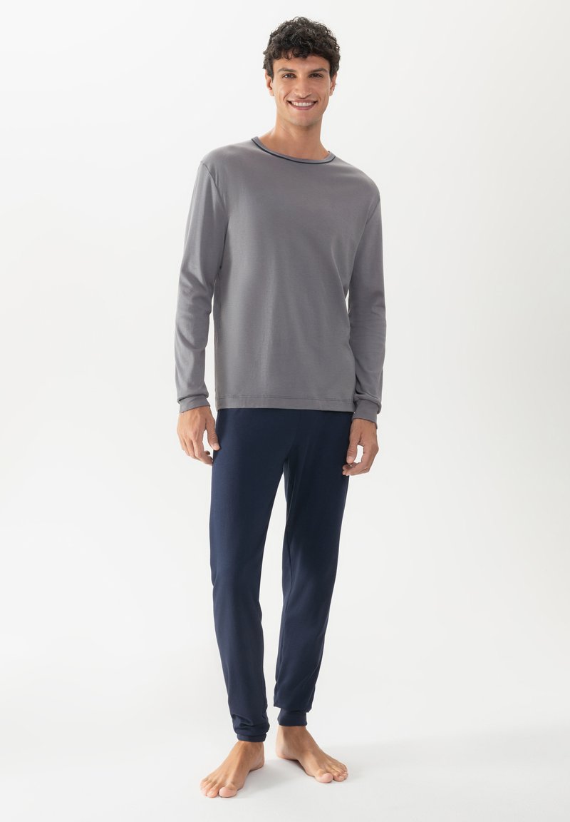 Grijs langemouwshirt met een marineblauwe halslijn, gecombineerd met marineblauwe broek. De stof lijkt zacht, met aansluitende manchetten en tapered benen.