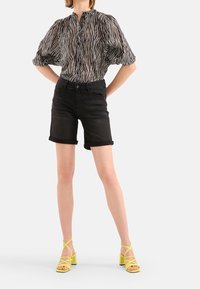 Černobílý pruhovaný top s knoflíkovým výstřihem, zkombinovaný s černými denimovými šortkami a žlutými sandály na podpatku se křížovými pásky.