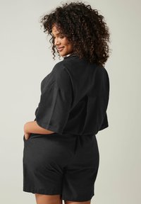 Mono de lino negro con mangas cortas, un corte holgado y bolsillos laterales. Presenta un escote alto y una cintura elástica para mayor comodidad.