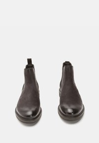 Botine Chelsea din piele neagră cu o textură netedă, vârf rotund, panouri elastice laterale și cusături contrastante la talpă. Design plat, fără embellishments.
