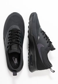 Une paire de baskets Nike Air Max noires montrées de dessus et de côté, avec des lacets et une semelle à coussin d'air visibles sur fond blanc.