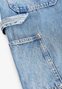 Tavan de denim bleu deschis cu margine pliată și un buzunar vizibil. Prezintă o textură subtilă și cusături clasice.