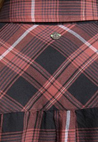 Röd och svart rutigt klänning med en texturerad tyg, som har en veckad kjol och en metallisk accentknapp på bröstet.