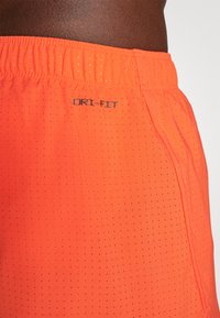 Lysoransje sportsjshorts laget av pustende, teksturert stoff med perforeringer, med elastisk liv både og Dri-FIT-merke.
