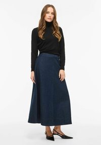 Długa spódnica maxi z ciemnoniebieskiego denimu o rozkloszowanym kroju, zestawiona z czarnym golfem i czarnymi czółenkami w szpic.