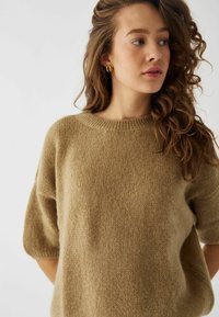 Sweter dzianinowy w miękkim beżu, z okrągłym dekoltem i krótkimi rękawami. Tekstura jest puszysta, podkreślająca casualowy design.