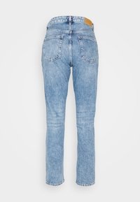 Jean en denim bleu clair avec une coupe droite, un design classique à cinq poches et un léger effet délavé, avec un patch en cuir à la taille.