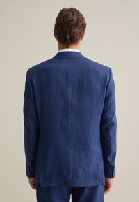 Chaqueta de traje de lino navy con una textura suave, abertura sencilla en la parte posterior y acentos de puños abotonados. Diseño limpio con un ajuste a medida.