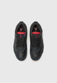 Schwarze Sportschuhe mit Obermaterial aus Leder und Textil, strukturierten Akzenten, schwarzen Schnürsenkeln, roten Details an der Zunge und einer weißen Laufsohle.